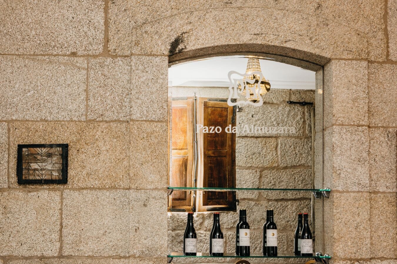 A stone wall with a wooden door and a glass shelf displaying wine bottles.