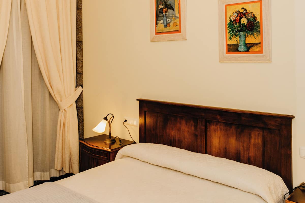 A bedroom with a bed, a nightstand, a lamp, a chandelier, and two framed pictures on the wall.