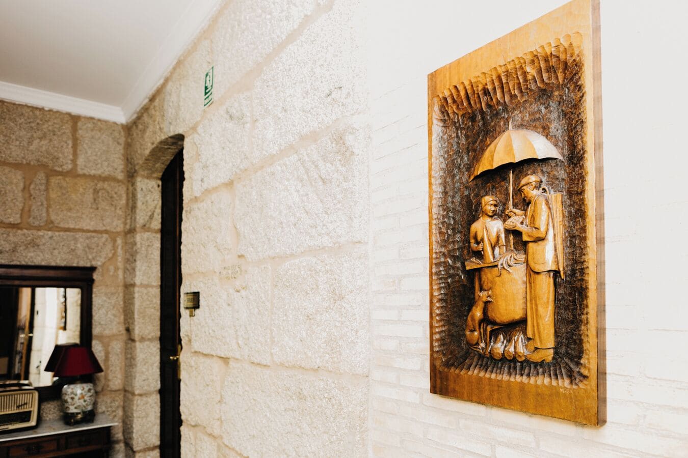 Un muro in pietra con un rilievo in legno scolpito raffigurante due figure, una lampada e una radio d'epoca.