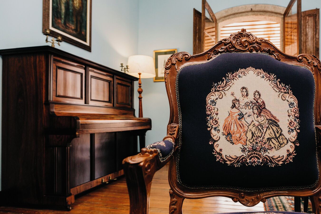 A room with a dark wooden piano, a chair with a detailed backrest, and a framed picture on the wall.