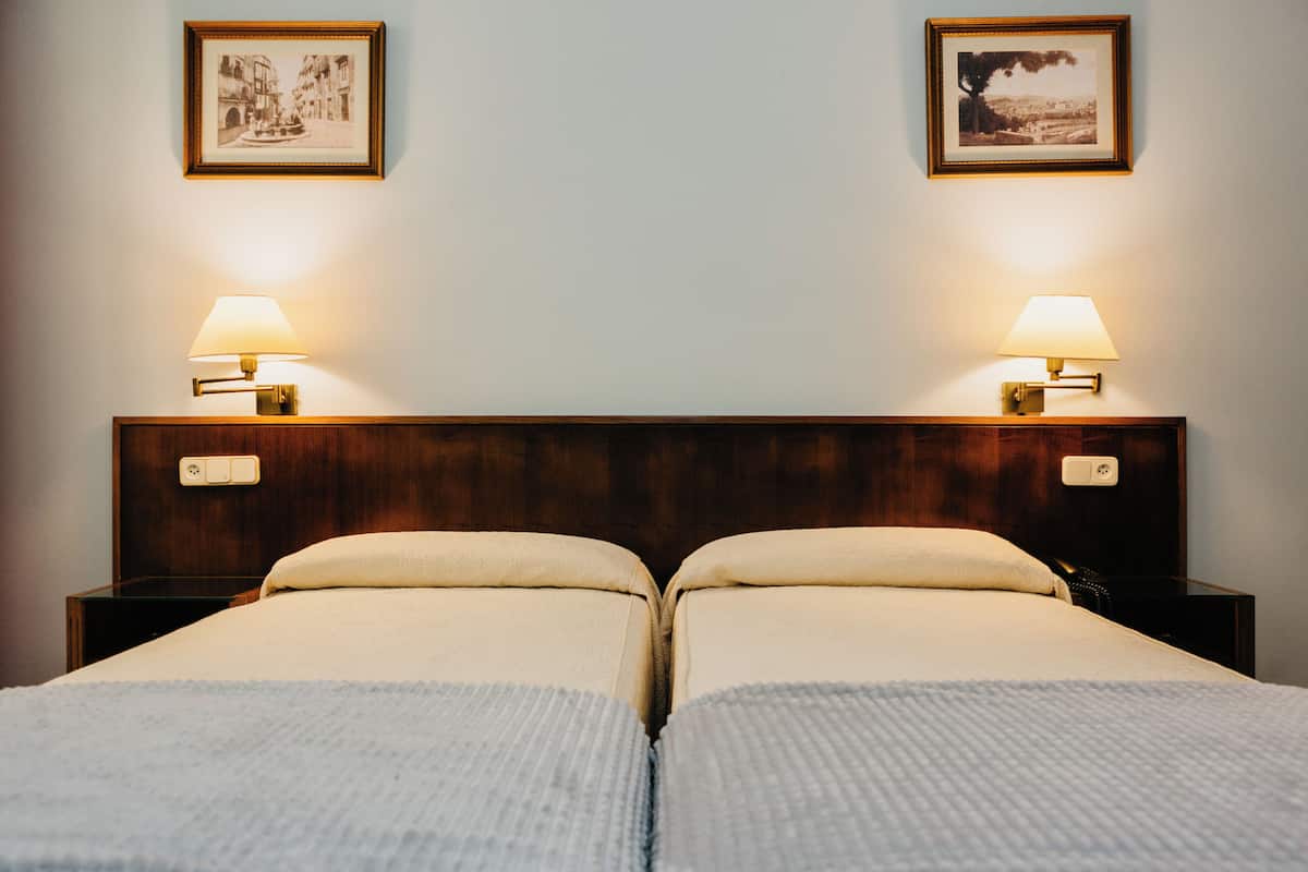 A double bed with two bedside tables, each with a lamp, framed pictures on the wall, and a wooden headboard.