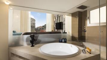 Une salle de bain moderne dotée d’une grande baignoire, d’une douche en verre et offrant une vue sur le Colisée grâce à une grande fenêtre.