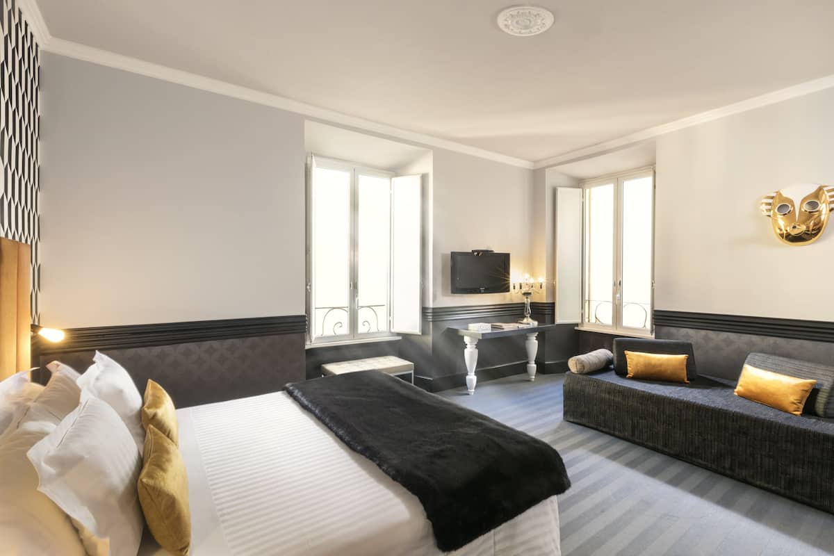 A hotel room with a bed, a sofa, a desk, and a TV.