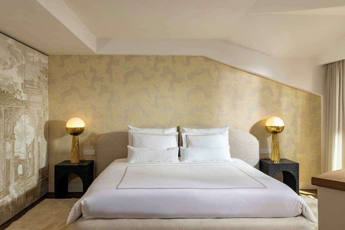 A hotel room with a large bed, two bedside lamps, and a patterned wallpaper.