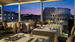 Un restaurante con mesas dispuestas para comer, amplias ventanas que ofrecen vistas del Coliseo, y una decoración de interiores moderna.