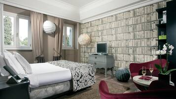 A hotel room with a bed, a TV, a bookshelf, and a red armchair.