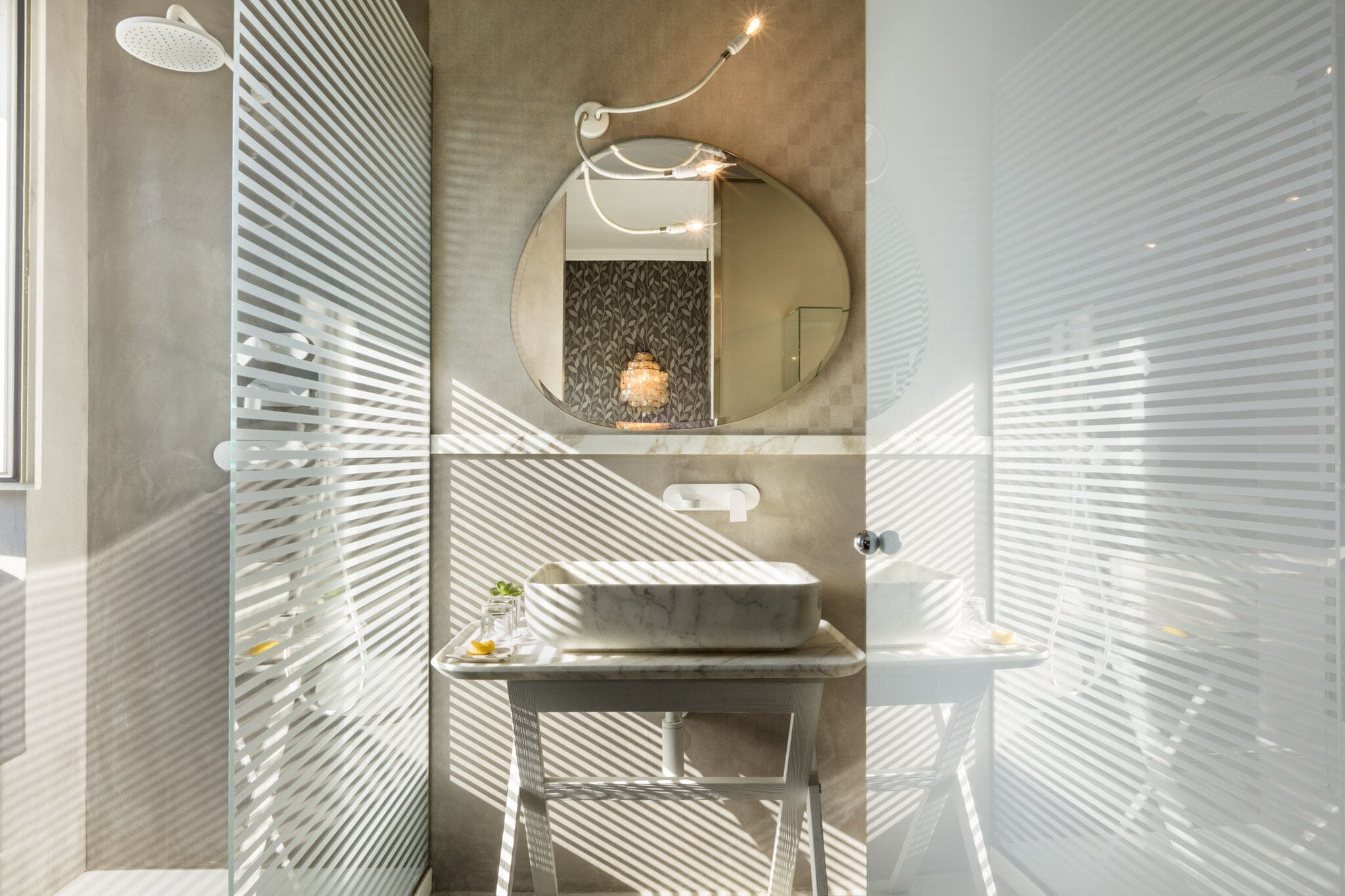 A modern bathroom with a round mirror, a marble sink, and a shower with a glass enclosure.