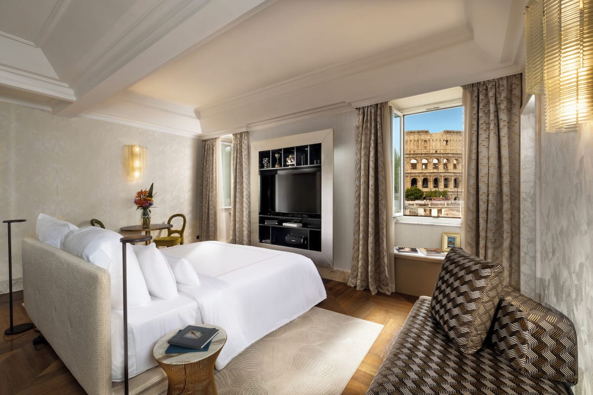 A hotel room with a bed, sofa, TV, and a window with a view of a historical building.