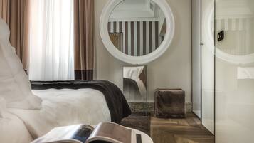 A hotel room with a bed, a round mirror, a small stool, and a book on the bed.