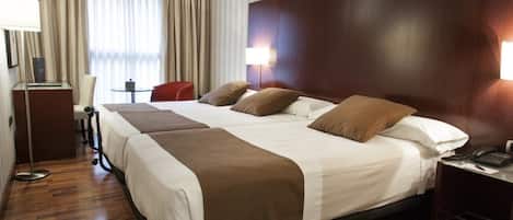 Habitación de hotel con una cama grande, dos mesitas de noche, un escritorio con silla, una lámpara y una ventana con cortinas.