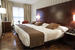 Une chambre d’hôtel avec un grand lit, deux tables de chevet, un bureau avec une chaise, une lampe et une fenêtre avec des rideaux.