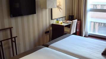 A hotel room with two beds, a desk with a chair, a television, and a window with curtains.