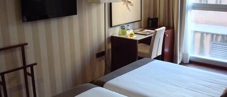 Habitación de hotel con dos camas, un escritorio con silla, televisor y ventana con cortinas.