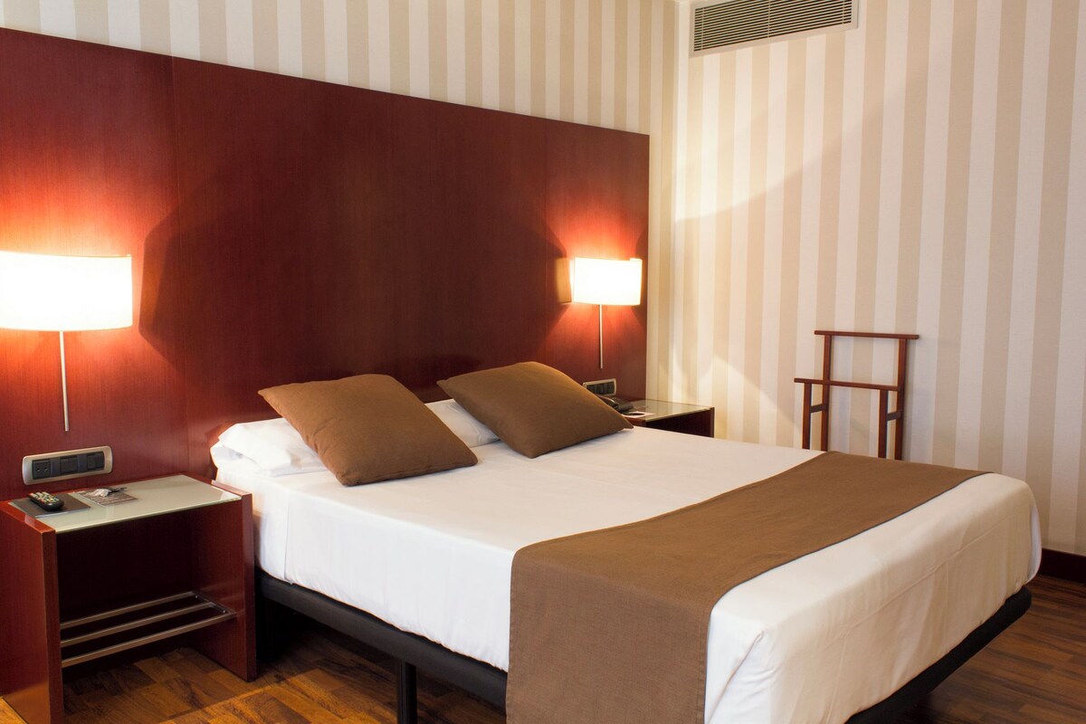 A hotel room with a large bed, two bedside lamps, a nightstand, and a wooden headboard.