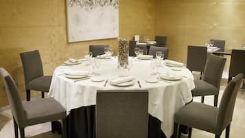 Un salón de conferencias con una mesa redonda dispuesta para una reunión, rodeada de sillas, y un cuadro abstracto grande en la pared.