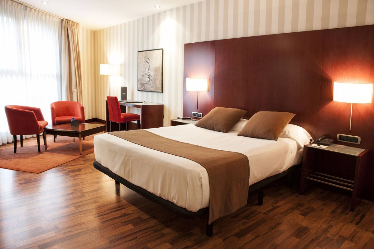 Ein Hotelzimmer mit einem großen Bett, zwei Nachttischen, einem Schreibtisch mit Stuhl und zwei Lampen.