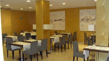 A restaurant with multiple tables and chairs, each set with white tablecloths and wine glasses.