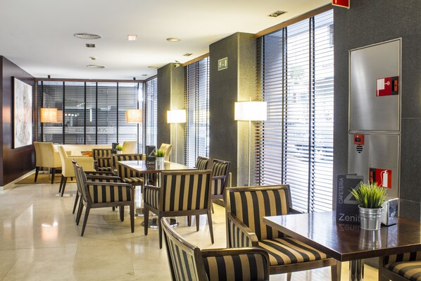 Un hall d'hôtel moderne avec un espace repas, des chaises à rayures et de grandes fenêtres équipées de stores.