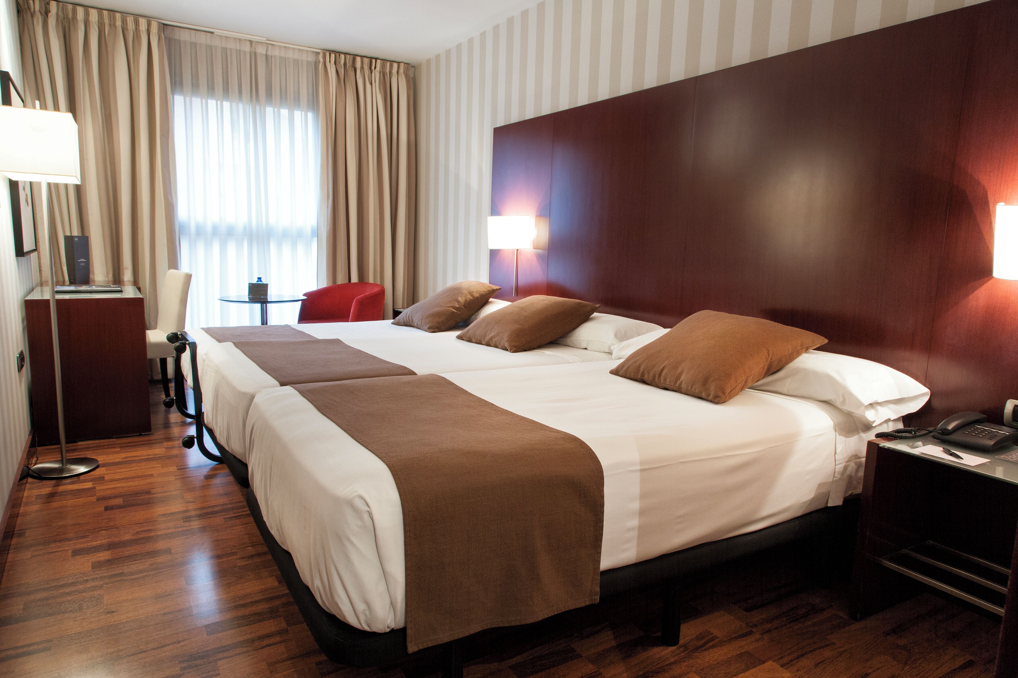 A hotel room with a large bed, bedside tables, a desk, a chair, and a lamp.