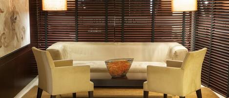 A modern living room with a beige sofa, two matching armchairs, a woven basket, and a wooden slatted wall with two hanging lamps.