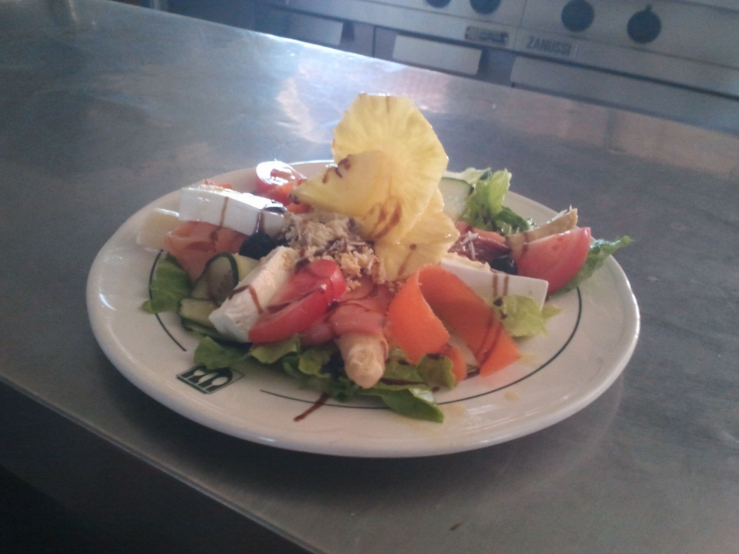 Un plato de ensalada mixta con diferentes verduras y una rodaja de piña.