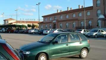 Un estacionamiento con varios coches, un edificio con ventanales arqueados y un letrero que dice 'Ristorante'.