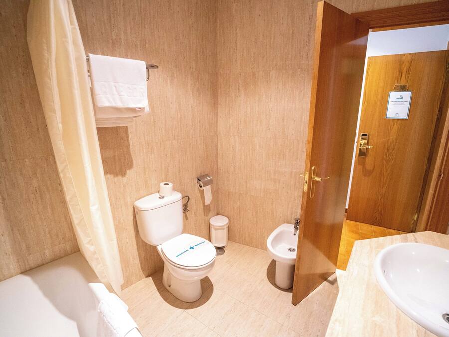 A bathroom with a toilet, bidet, sink, and a shower curtain.