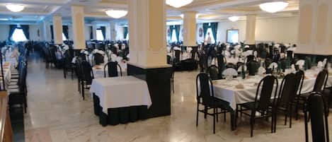 Un salón de banquetes con filas de mesas y sillas, grandes columnas y candelabros.