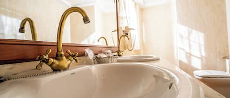 Un baño con un lavamanos grande de color blanco, un grifo dorado y un espejo encima.