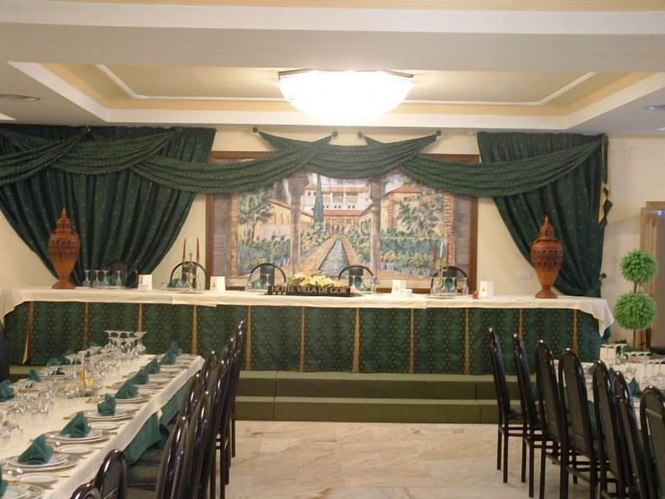 Een balzaal met een lange tafel gedekt voor een maaltijd, met groene gordijnen en een muurschildering op de achterwand.