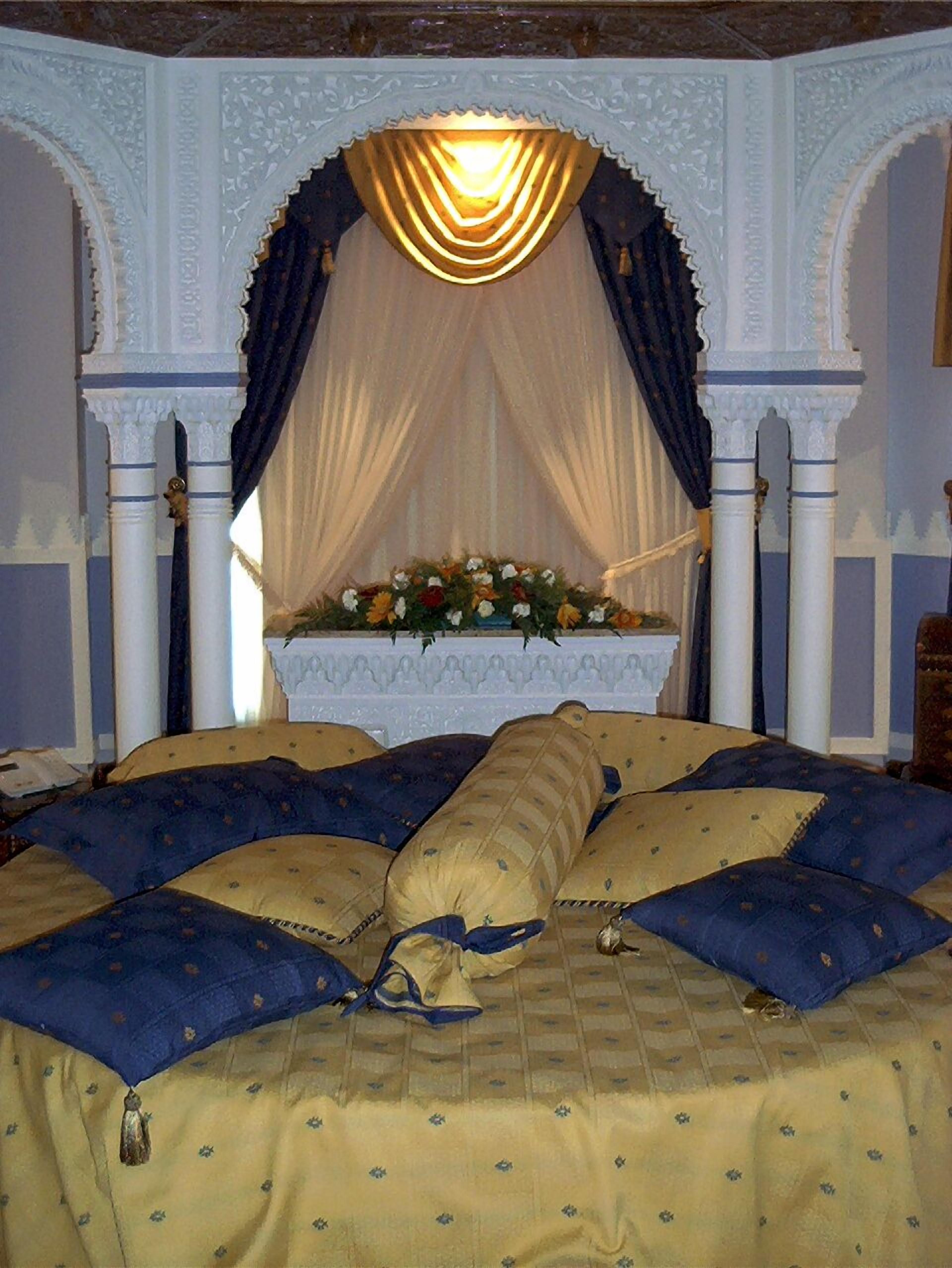 A bed with a floral arrangement in the center, surrounded by ornate white columns and draped fabric.