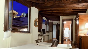 A room with a wooden ceiling, a bed, a desk with a computer, and a view of a building outside. - Casa del Capitel Nazari Hotel (Granada)