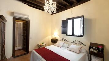 Un dormitorio con cama, candelabro, ventana y mesita de noche.