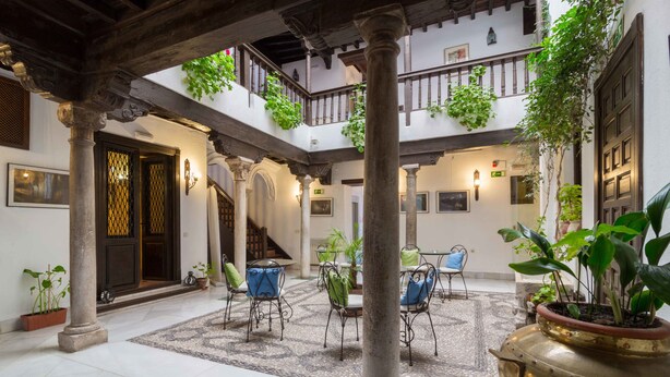 A spacious courtyard with a central seating area, columns, and potted plants. - Casa del Capitel Nazari Hotel (Granada)