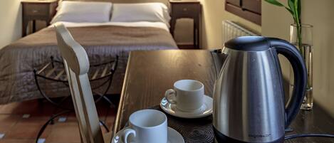 A hotel room with a bed, bedside lamps, a table with a kettle, cups, and a chair.