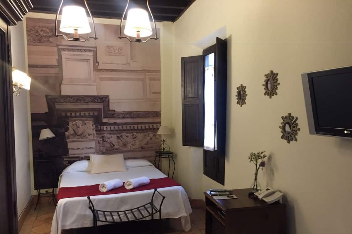 A hotel room with a bed, a desk, a chair, a TV, and decorative wall elements.
