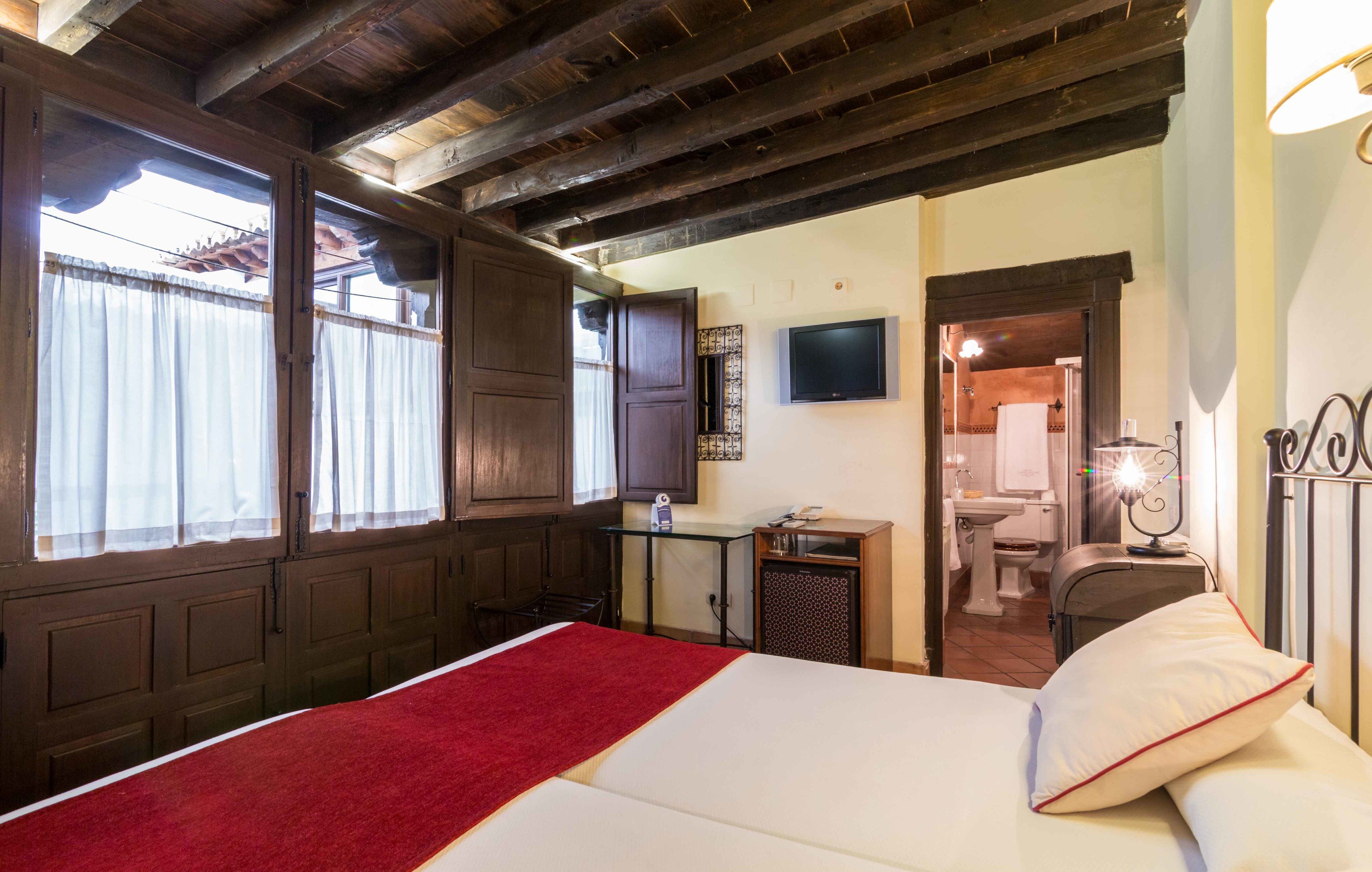 A hotel room with a bed, a desk, a television, and a bathroom visible through an open door.