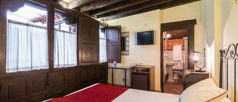 Habitación de hotel con cama, escritorio, televisión y baño visible a través de una puerta abierta.