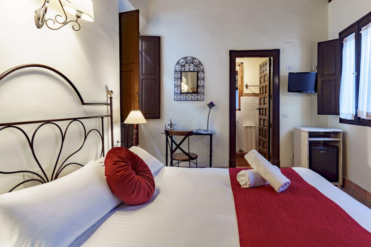 A hotel room with a bed, a desk, a TV, and a bathroom visible through an open door.