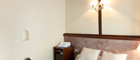 Una habitación de hotel con una cama, mesita de noche, lámpara y una pequeña mesa cubierta con un paño rojo.