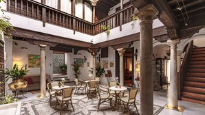 A spacious courtyard with a central seating area, columns, and a staircase leading to an upper level. - Casa del Capitel Nazari Hotel (Granada)