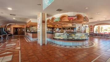 A spacious hotel lobby with a central food counter, seating areas, and a clear path leading to the entrance.