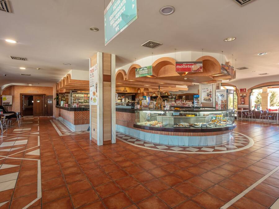 Un amplio vestíbulo de hotel con un mostrador de comida central, zonas de estar y un camino despejado hacia la entrada.