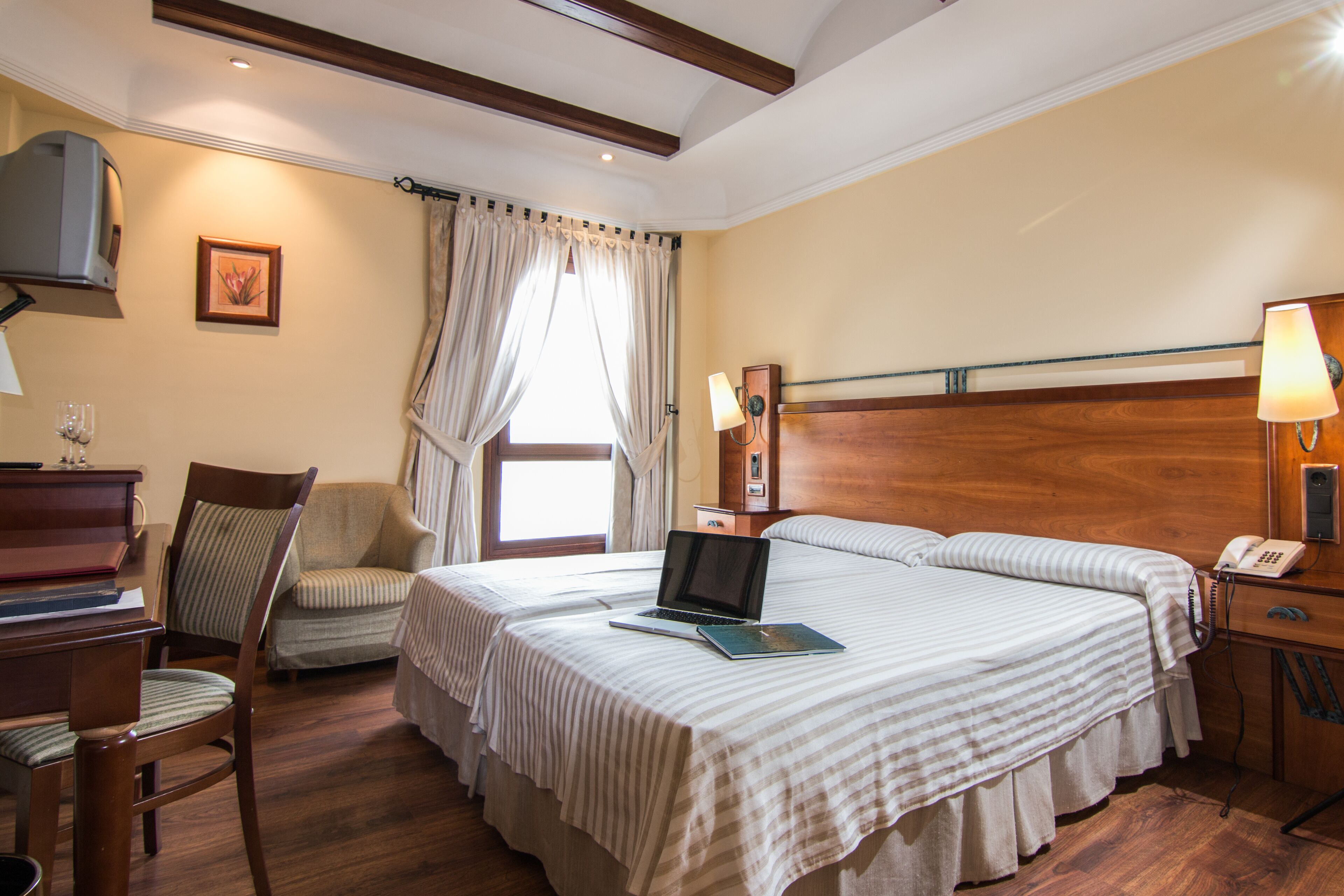 Habitación de hotel con dos camas, un escritorio, una computadora portátil, una silla, una lámpara y un teléfono.