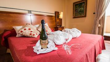 Una cama bien tendida con un edredón rojo, una botella de vino y una copa de vino encima.