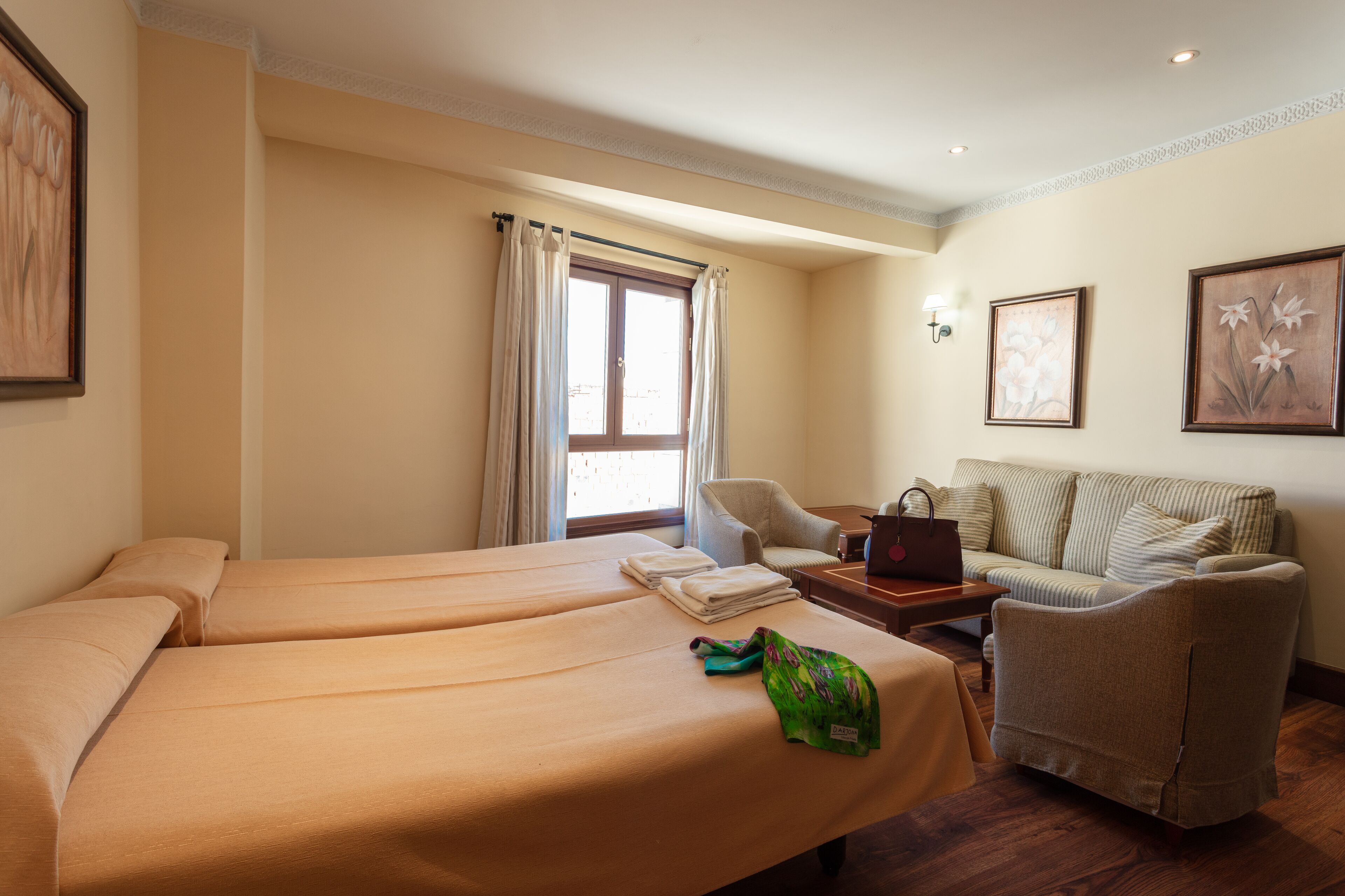 Habitación de hotel con dos camas, un sofá, una silla, una mesa y una ventana con cortinas.