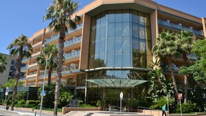 A multi-story hotel with a glass facade, palm trees, and a covered entrance. - Hotel California Palace (Salou)