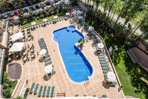 Vista aérea de un área de piscina de hotel con sillones de sol, una piscina central y follaje circundante.