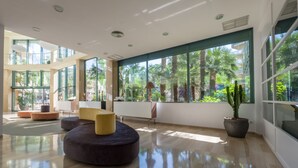 A spacious lobby with a modern design, featuring a large seating area, a potted plant, and large windows offering a view of the outdoors. - Hotel California Palace (Salou)