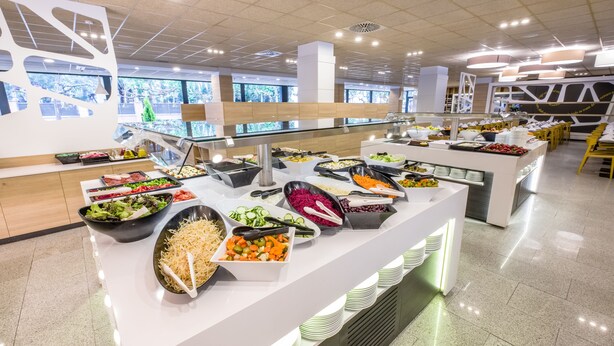 A buffet with various food options, a modern interior design, and large windows. - California Garden (Salou)